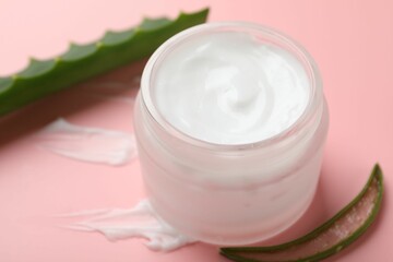 Moisturizing cream with extract of aloe vera in jar and cut leaves on pink background, closeup