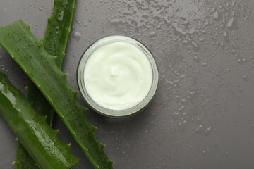 Moisturizing cream with extract of aloe vera in jar, cut leaves and water drops on grey background, flat lay. Space for text