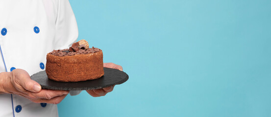 Professional pastry chef with delicious chocolate cake on light blue background, closeup. Space for text
