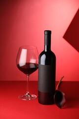 Tasty wine in bottle, glass and flower on red background