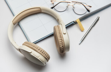 Wireless headphones, planner, eyeglasses and pen lying on white table