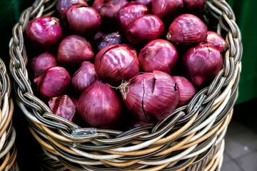 A close-up of a wicker basket filled with vibrant red onions, showcasing their rich color and...