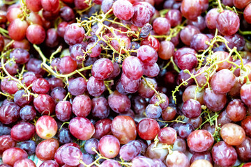 A close-up, high-angle shot of a pile of ripe, red grapes with a slightly blurred background. The image showcases the grapes' vibrant color and texture.