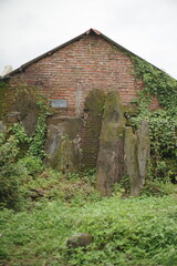 An old brick house with mossy rock formations, partly covered by vines and lush greenery.