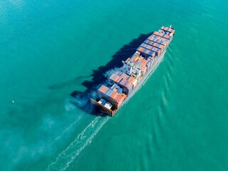 Aerial view of a container ship transporting goods across the ocean. The vessel is moving quickly,...