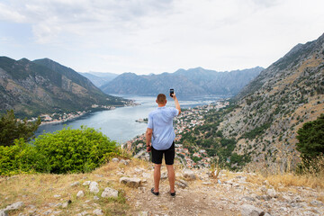 Fototapeta premium A man takes a photo of a stunning bay view from a mountaintop, capturing the picturesque landscape with his phone