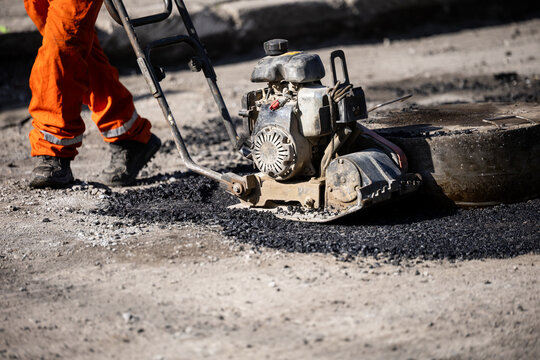 Workers repairing asphalt with machinery on a construction site during daylight hours in an urban area