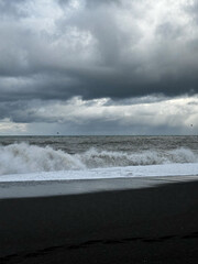 Crashing waves on black sand beach under storm clouds