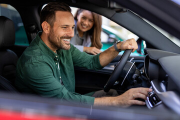 Beautiful young woman in classic suit is smiling while showing a car in a motor show. Handsome...