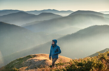 Young man wearing a blue jacket hiking on a mountain trail at sunrise, with low clouds filling the...