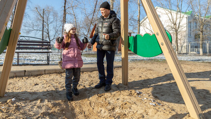Grandfather playing with his granddaughter on the playground in the park in winter