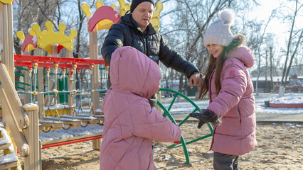 Grandfather with grandchildren playing on the playground on a cold winter day