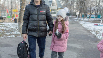 Grandfather walks with his granddaughters after school in the park in sunny winter day