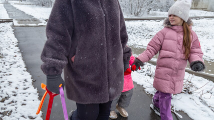 Grandmother and girls walk along a snowy street in winter