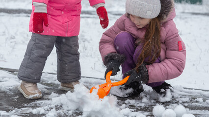 Two little girls in colorful clothes play outdoors during a snowfall.