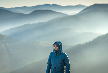 Young man with stubble, wearing a blue jacket, looking out at the breathtaking view from the top of...