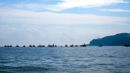 雲がかった青空の下、穏やかな青い海面に浮かぶ漁船団