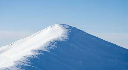 Serene snowy mountain peak under a clear blue sky, bathed in gentle sunlight