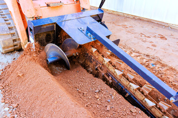 Heavy trencher machinery operates to create trench in sandy soil for construction purposes