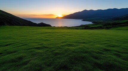 Fototapeta premium Scenic sunset over a grassy meadow overlooking the sea and mountains
