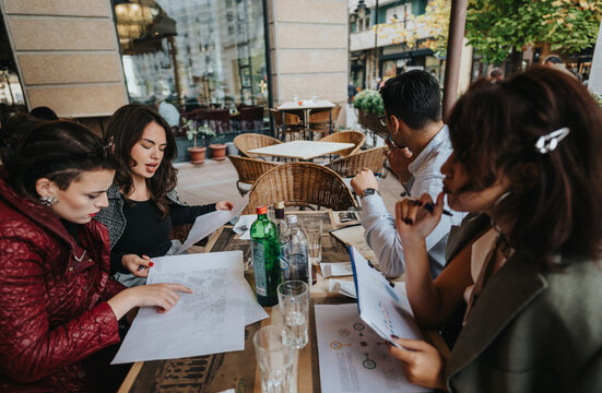 A diverse group of businesspeople engaged in a team meeting outdoors at a cafe. They are reviewing documents and discussing project strategies, fostering a collaborative atmosphere in a relaxed