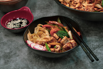Vegan stir fry with tofu peppers and rice noodles in black bowl with chopsticks, copy space