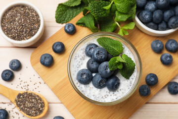 Delicious chia pudding with blueberries and mint in glass on wooden table, flat lay