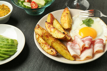 Tasty brunch. Fried egg, potato, bacon and cut avocado on dark textured table, closeup