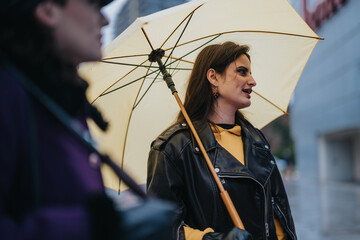 Two women share a moment in an urban cityscape while one carries an umbrella during rainy weather....