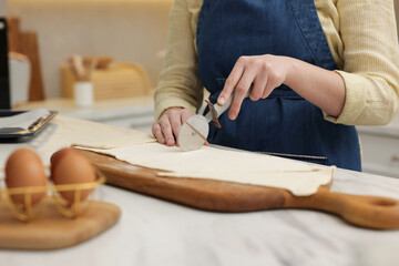 Woman cutting dough at light marble table indoors, closeup. Making croissants