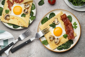 Delicious crepes with eggs, bacon and mushrooms served on grey table, flat lay. Breton galette