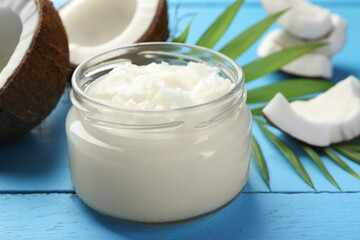 Organic coconut cooking oil in jar, pieces of fruit and green branch on light blue wooden table, closeup