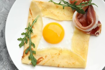 Delicious crepe bretonne with bacon and arugula on grey textured table, top view