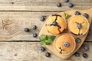 Delicious muffins with blueberries and mint on wooden table, flat lay. Space for text