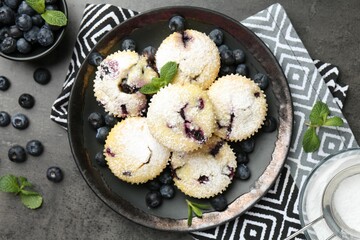Delicious muffins with blueberries, powdered sugar and mint on dark textured table, flat lay