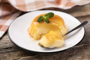 Delicious pudding with caramel sauce and mint served on wooden table, closeup