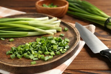 Fresh green onions and knife on wooden table, closeup