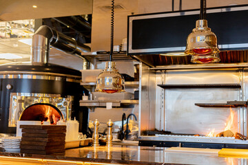 Well-equipped, modern kitchen in a restaurant or cafe, The kitchen features stainless steel appliances, cooking utensils, shelves, and a wood-fired oven, suggesting a high-end, professional.
