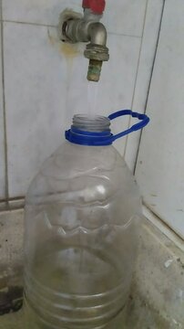 Un primer plano de una botella grande llen&aacute;ndose de agua en una batea o lavadero. Video Vertical.
