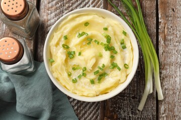 Tasty mashed potato with green onion in bowl and spices on wooden table, flat lay