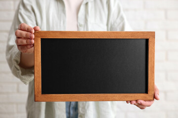 Woman holding blank small blackboard indoors, closeup