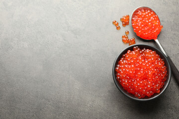 Tasty red caviar in bowl and spoon on grey table, top view. Space for text