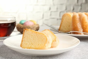 Pieces of delicious bundt cake, Easter eggs and tea on gray table, closeup