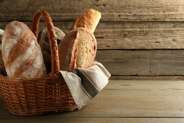 Different loaves of fresh bread in wicker basket on wooden table, space for text