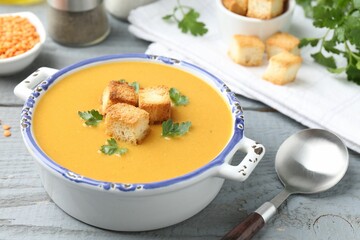 Delicious lentil cream soup served with croutons on grey wooden table, closeup