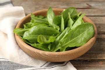 Fresh green sorrel leaves in bowl on wooden table, closeup