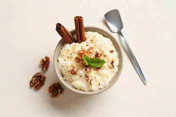 Delicious rice pudding with walnuts, cinnamon, mint and spoon on white table, flat lay