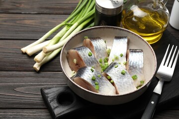 Pieces of delicious herring with green onions served on black wooden table, closeup