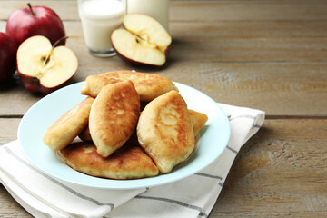 Delicious fried pyrizhky (stuffed pies) with apples and milk on wooden table. Space for text