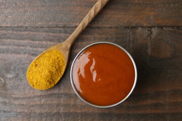 Tasty curry sauce in metal dish and powder on wooden table, top view